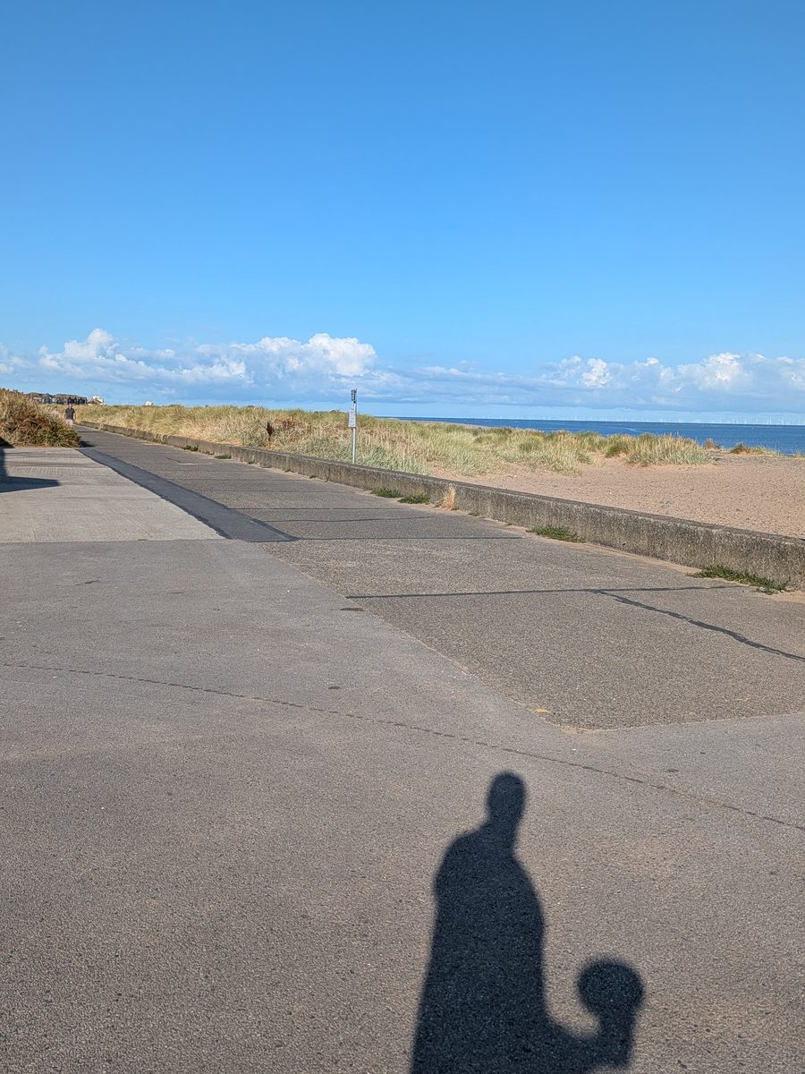 The exposed concrete coastal path at Fleetwood Promenade parkrun, with dunes, beach and offshore wind turbines visible